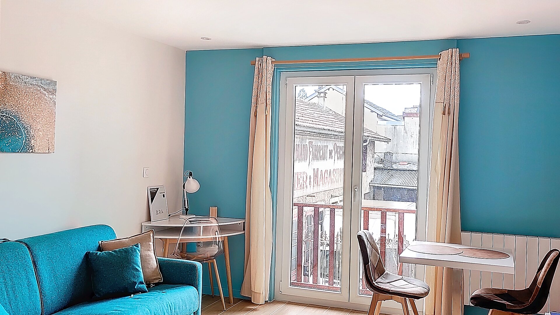 Séjour lumineux avec canapé turquoise et vue sur les toits d'Oyonnax